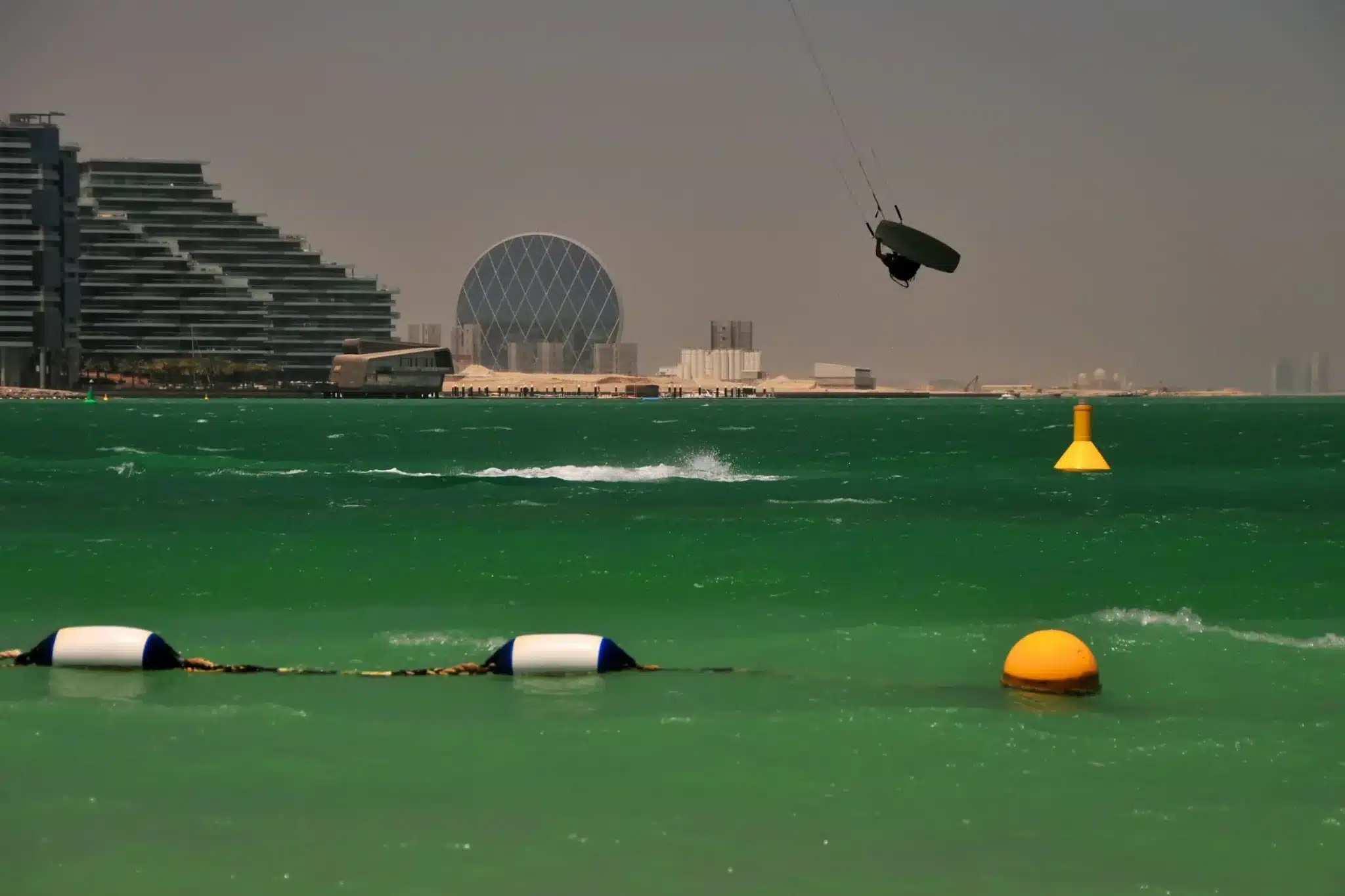 Kitesurfing along the coastline is a thrilling outdoor activity in Abu Dhabi with urban scenery in the background.