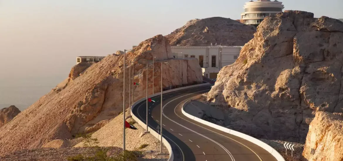 Malerische Serpentinenstraße, die zum Gipfel des Jebel Hafeet in Al Ain, Vereinigte Arabische Emirate, führt, umgeben von einer felsigen Wüstenlandschaft.