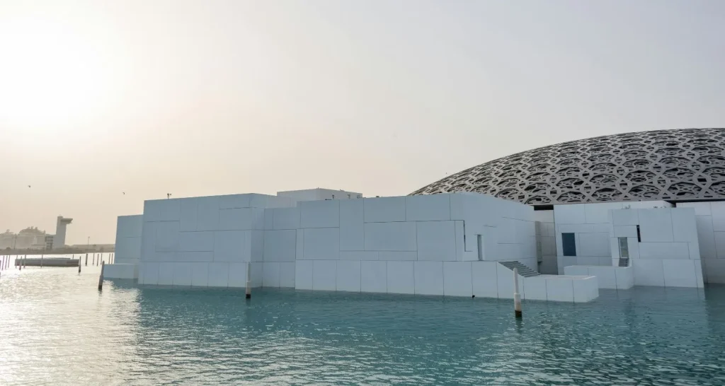 Modern architecture of the Louvre Abu Dhabi museum with its iconic dome and water surroundings at sunset.