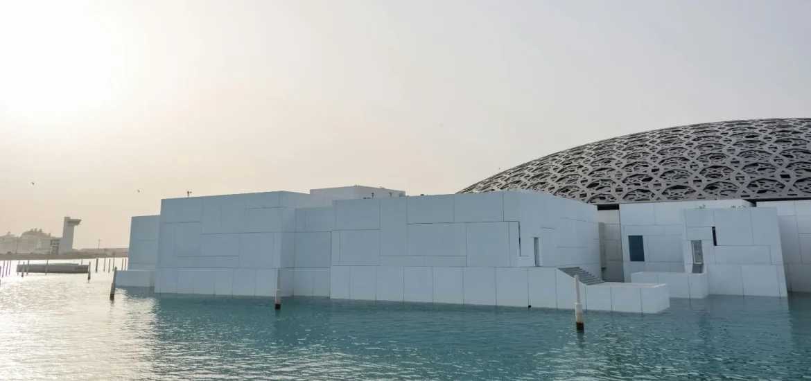 Die moderne Architektur des Louvre Abu Dhabi Museums mit seiner ikonischen Kuppel und der Wasserlandschaft bei Sonnenuntergang.