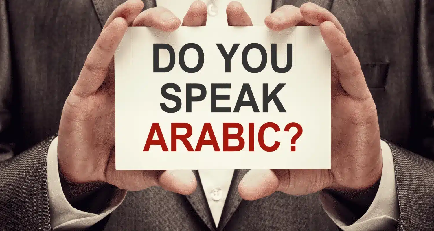 A man holding a board that says, "Do you speak Arabic?
