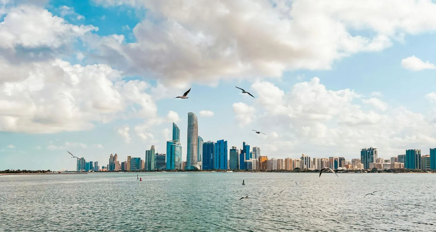 Skyline of Abu Dhabi with seagulls flying over the Arabian Gulf.