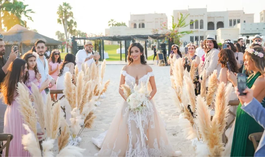 Braut schreitet den Gang hinunter im Al Maya Island Resort, umgeben von Pampasgras und Gästen einer luxuriösen Hochzeit in Abu Dhabi.