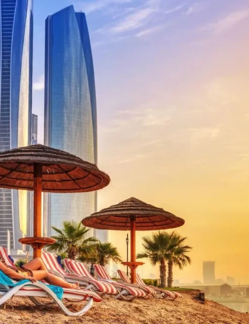 Eine Frau entspannt sich am Strand von Abu Dhabi mit Blick auf moderne Wolkenkratzer bei Sonnenuntergang.