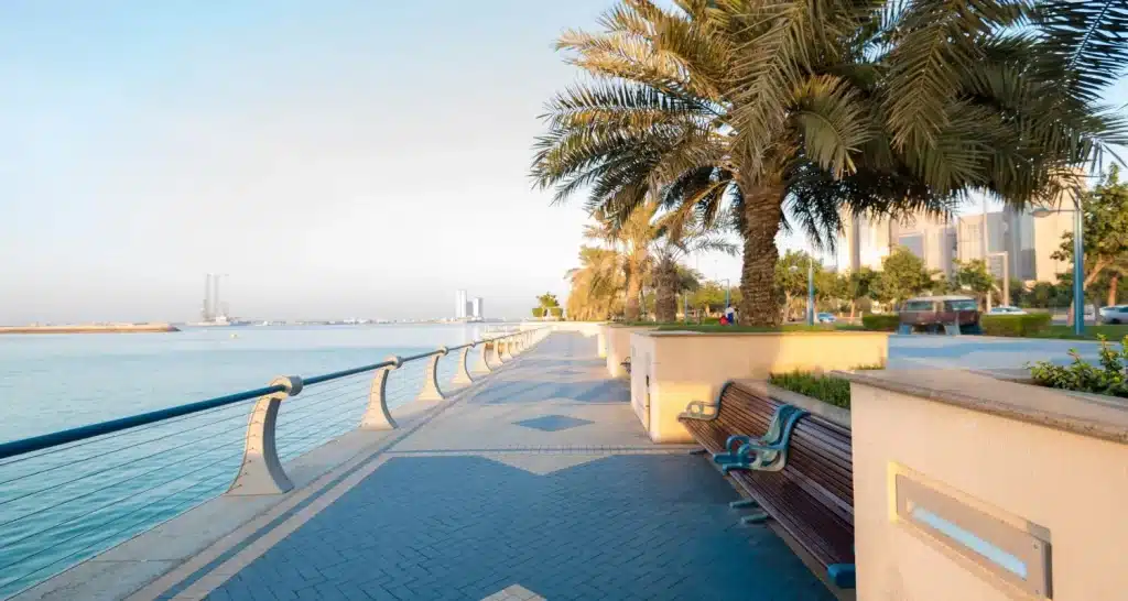 Malerischer Blick auf die mit Palmen und Bänken gesäumte Promenade der Abu Dhabi Corniche.