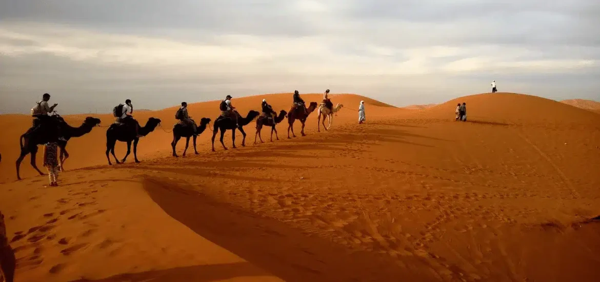 Eine Reihe von Menschen, die am Nachmittag auf einer Wüstensafari auf Kamelen reiten.