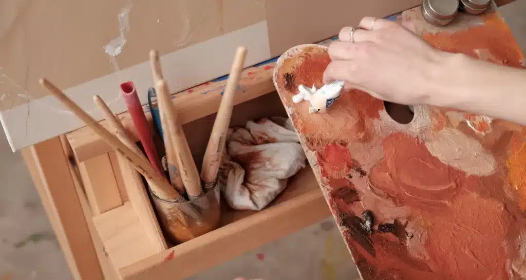 Nahaufnahme der Hand eines Künstlers, der während einer Malstunde Farben auf einer Palette mischt.