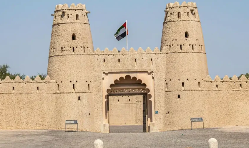 Vorderansicht der Festung Al Jahili in Al Ain mit der Flagge der Vereinigten Arabischen Emirate, die über den Eingangstürmen weht.