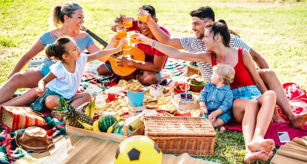 Familie beim Picknick auf der Wiese im Green Mubazzarah Park mit Obst und Spielen.