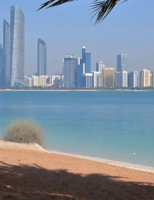 Blick auf die Strände von Abu Dhabi mit Skyline und türkisfarbenem Golfwasser, eingerahmt von Palmen.