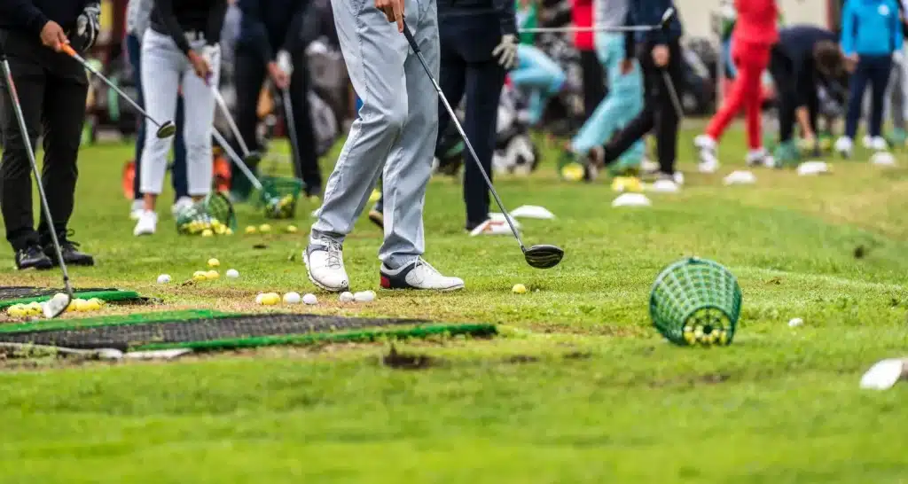 Spieler trainieren auf einer belebten Driving Range, auf der Golfbälle verstreut liegen.