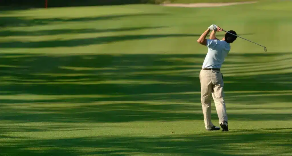 Ein Golfer macht an einem sonnigen Tag einen Schwung auf einem grünen Fairway.