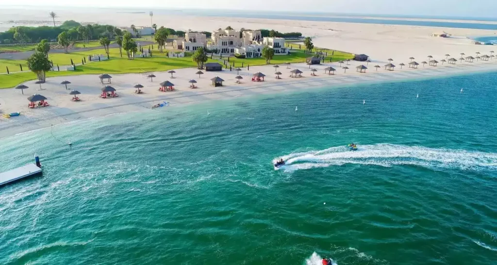 Der Strand von Al Maya Island in Abu Dhabi mit weißem Sand, ruhigem türkisfarbenem Meer und Jetskis in Ufernähe.