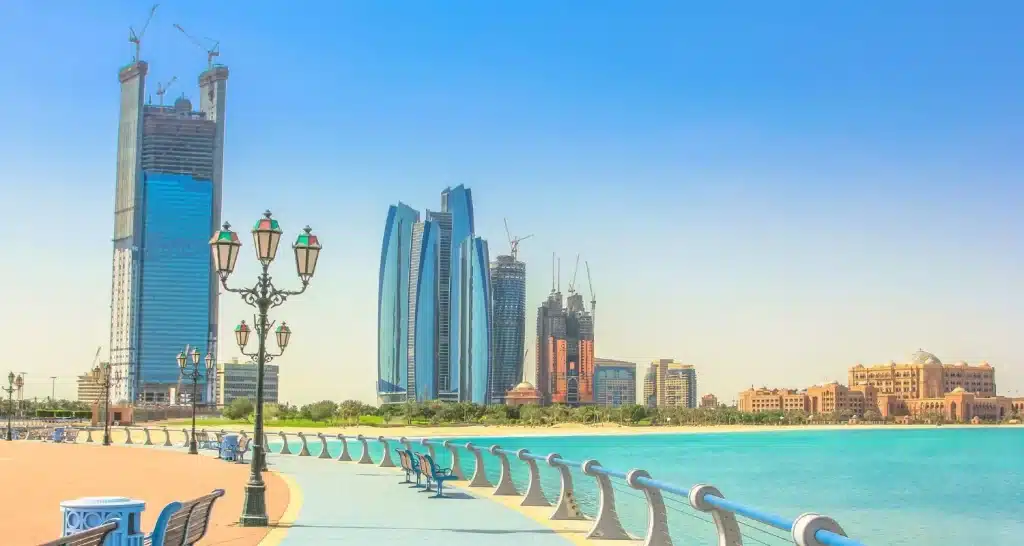 Corniche Beach in Abu Dhabi mit Promenade, blauem Wasser und der Skyline der Stadt im Hintergrund.