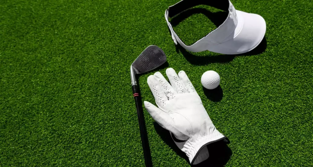 Golfausrüstung, darunter ein Handschuh, ein Schläger und ein Ball, auf dem leuchtend grünen Rasen des Abu Dhabi City Golf Club.