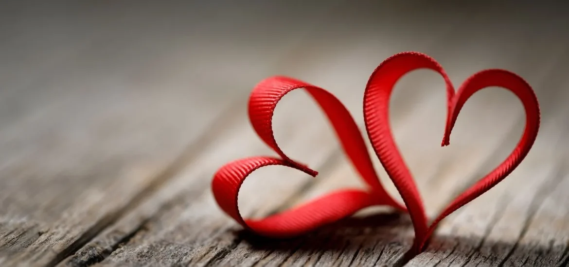 Rotes Band in Form von zwei Herzen auf einer hölzernen Oberfläche, die einfache Gefühle zum Valentinstag symbolisieren