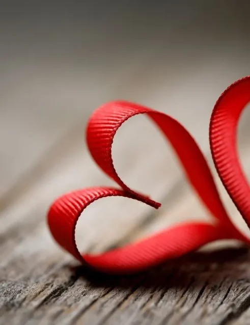 Rotes Band in Form von zwei Herzen auf einer hölzernen Oberfläche, die einfache Gefühle zum Valentinstag symbolisieren