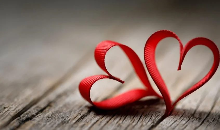 Rotes Band in Form von zwei Herzen auf einer hölzernen Oberfläche, die einfache Gefühle zum Valentinstag symbolisieren