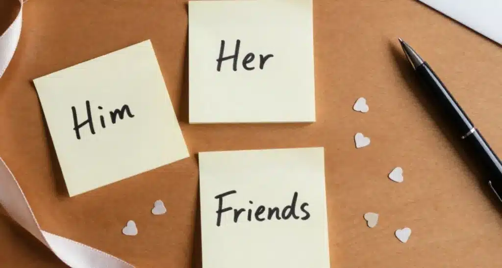 Drei Haftnotizen mit der Aufschrift "Er", "Sie" und "Freunde" auf einem Schreibtisch, auf denen die Valentinstagsnachrichten nach Beziehung geordnet sind